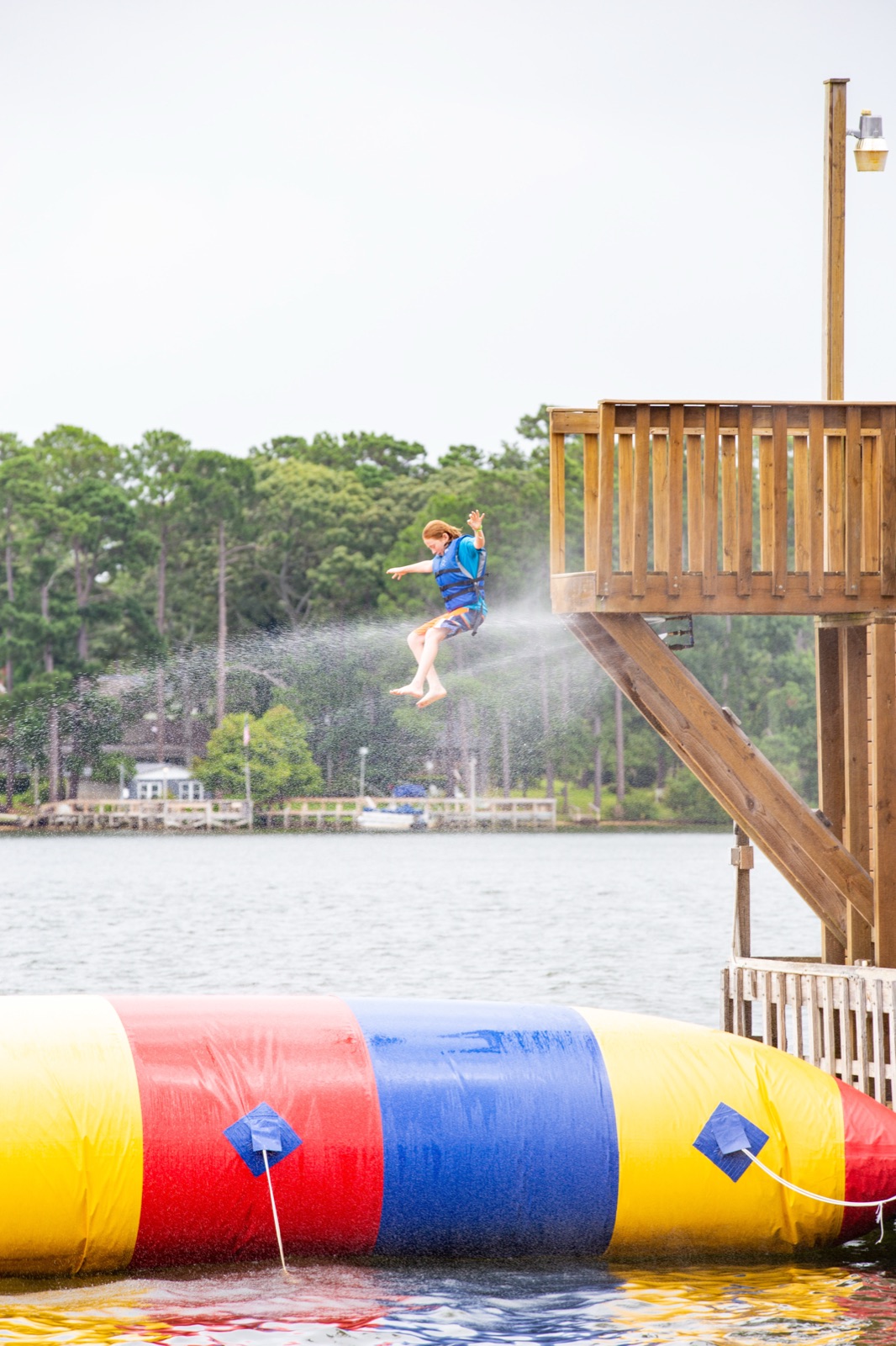 Camper in a life jacket launching off a water blob into the lake