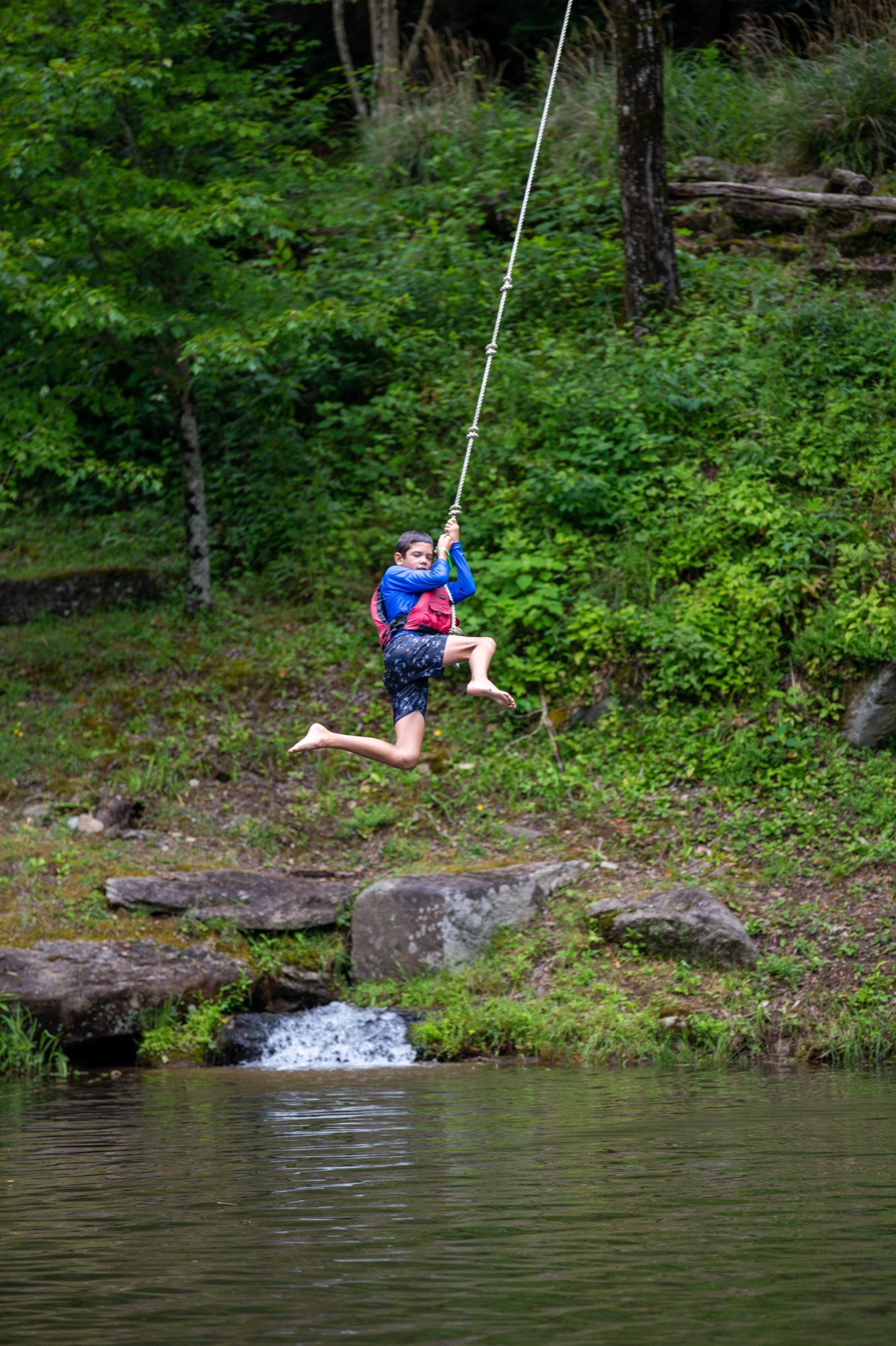Camper in a life jacket swinging out over the water on a rope swing