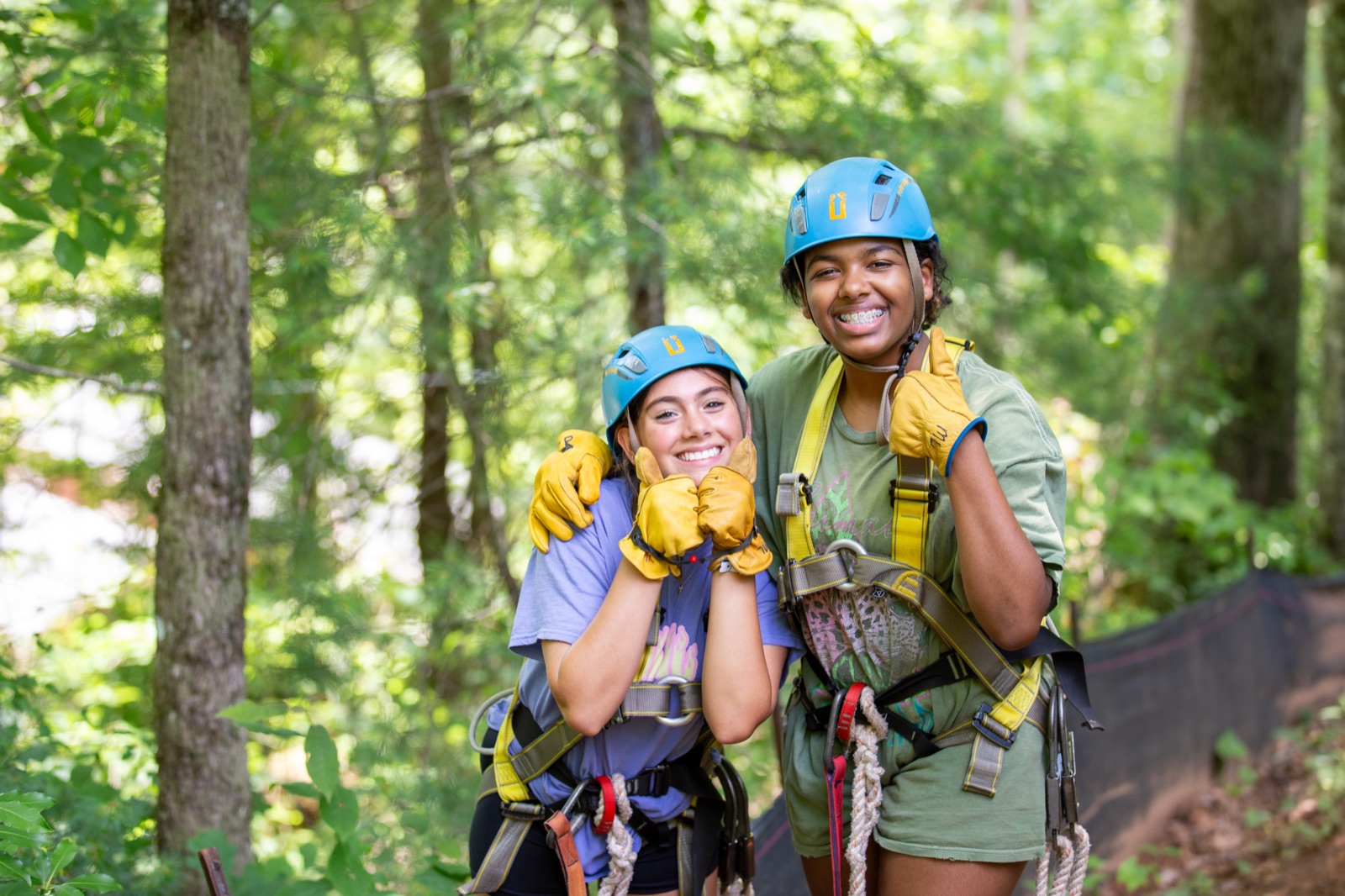 Two smiling campers in climbing helmets and harnesses on the zipline course