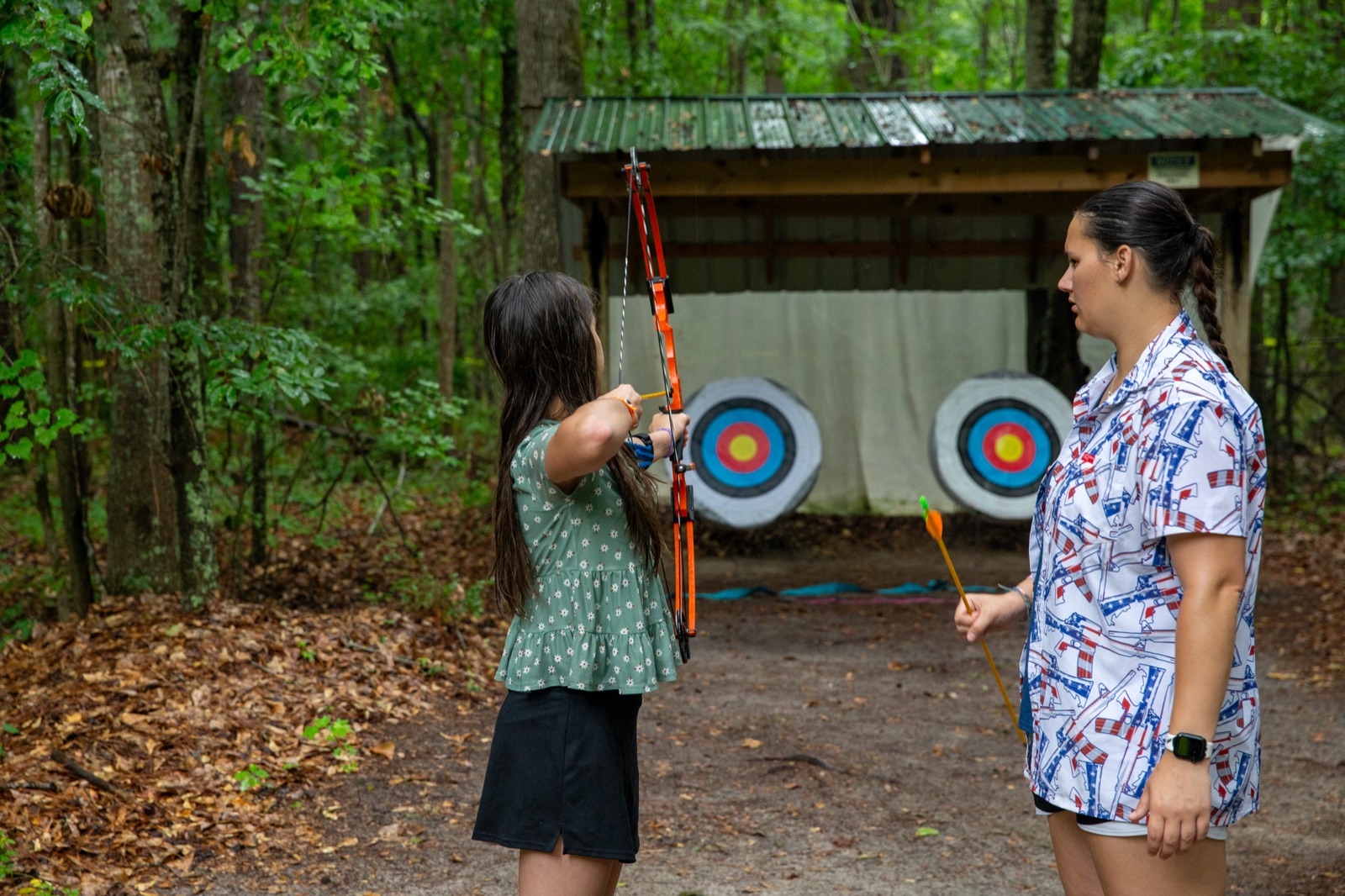 Camper drawing a bow at the archery range as an instructor looks on
