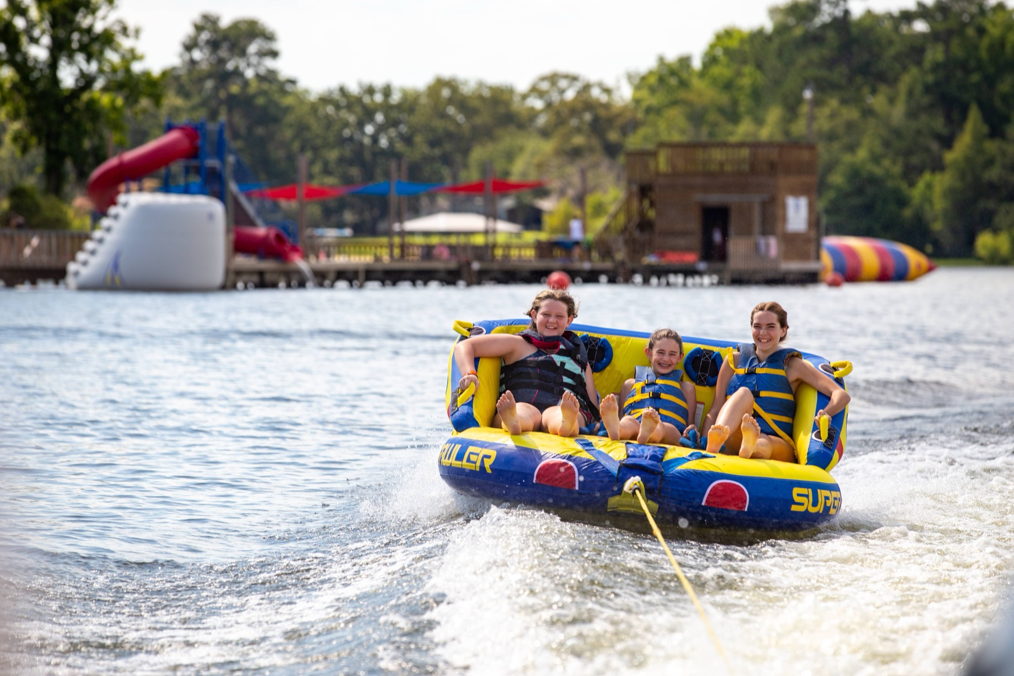 3 children are on a tube in the lake being pulled by boat.