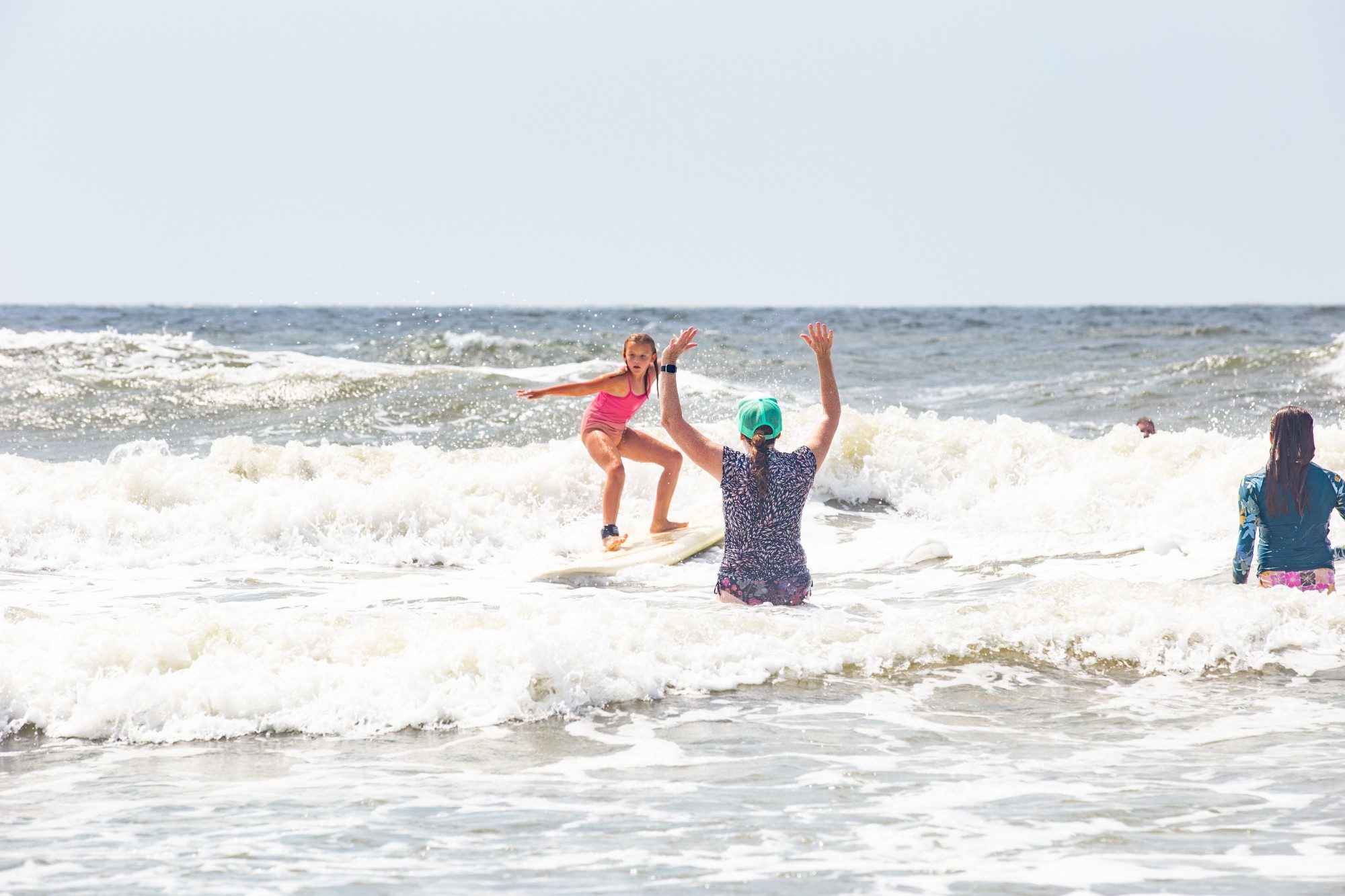 Camper standing up on a surfboard in the waves as an instructor cheers